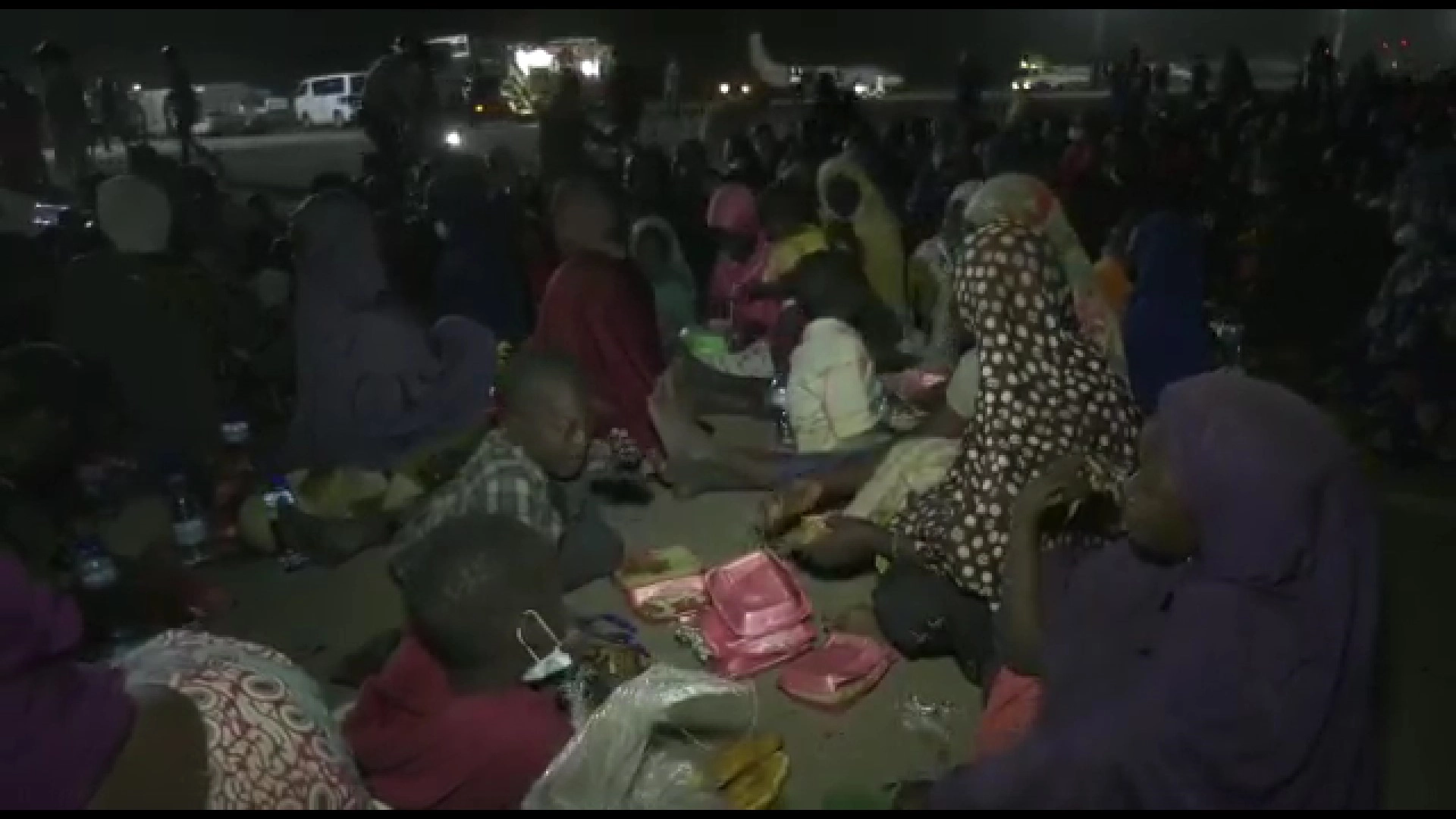 Niger nationals on Niamey's airport tarmac eating after being repatriated from Senegal